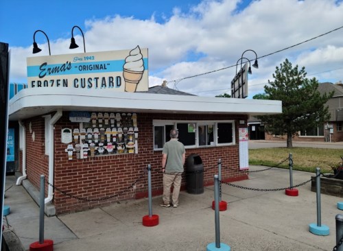 A person stands in front of a vintage frozen custard stand with a sign reading "Erma's Original Frozen Custard."