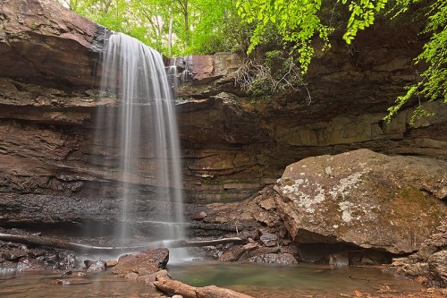 A serene waterfall cascades over rocky cliffs, surrounded by lush green foliage and a tranquil pool below.