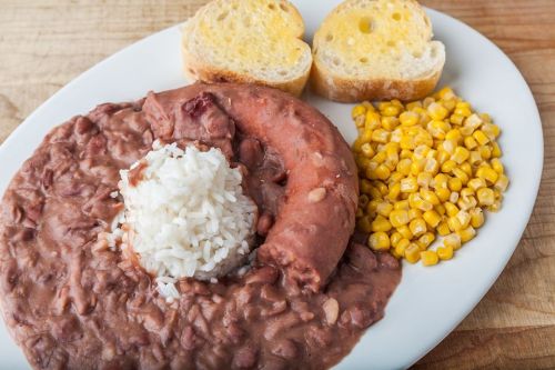 A plate with rice, red beans, sausage, corn, and two slices of buttered bread on a wooden surface.