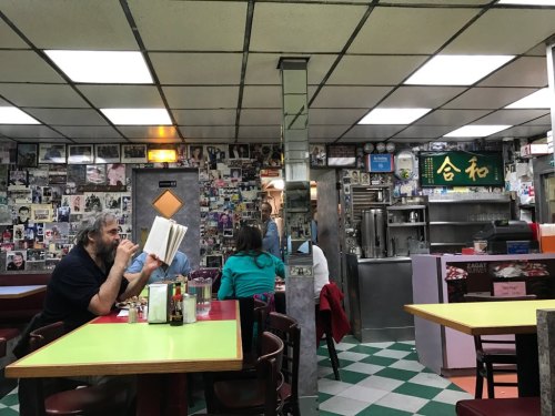 A cozy diner with colorful tables, patrons reading, and walls adorned with black-and-white photos.
