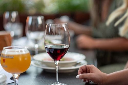 A close-up of a red wine glass on a table, with a beer glass and blurred diners in the background.