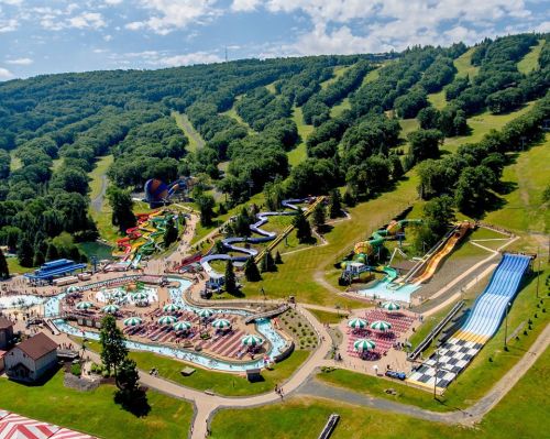 Aerial view of a vibrant water park with slides, pools, and green hills in the background on a sunny day.