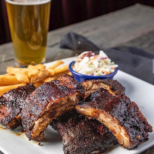 A plate of smoky ribs with coleslaw and fries, accompanied by a glass of beer.