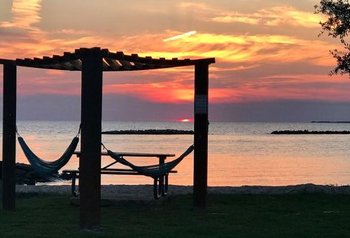 A serene beach scene at sunset, featuring a hammock under a wooden pergola with vibrant orange and pink skies.
