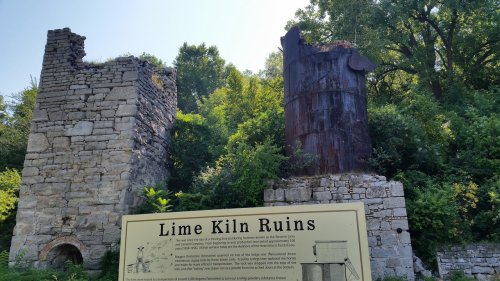 Ruins of lime kilns surrounded by greenery, with a sign reading "Lime Kiln Ruins" in the foreground.