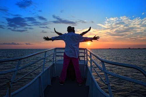 Silhouetted figures on a boat with arms outstretched against a vibrant sunset over the water.