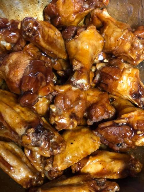 A close-up of cooked chicken wings coated in a glossy, dark sauce, arranged in a large bowl.