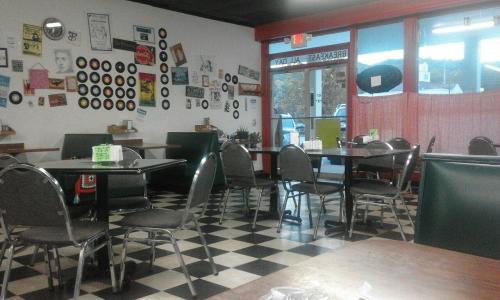 A cozy diner interior with checkered floors, empty tables, and walls decorated with records and vintage posters.