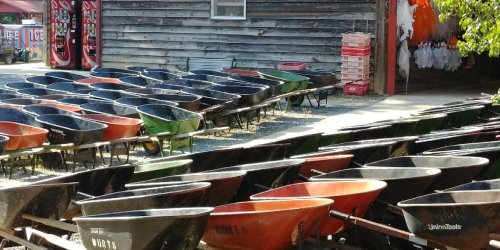 A row of colorful wheelbarrows lined up outside a rustic wooden building.