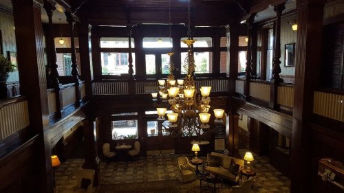 Elegant hotel lobby with wooden beams, a grand chandelier, and cozy seating areas, illuminated by natural light.