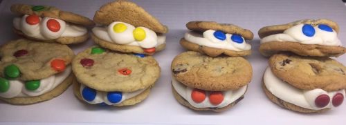 A row of cookie sandwiches filled with white frosting and colorful candy pieces, arranged neatly on a white surface.