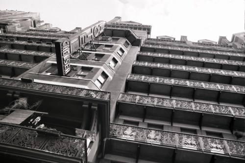 Black and white photo of a tall building with ornate balconies and a vintage hotel sign.
