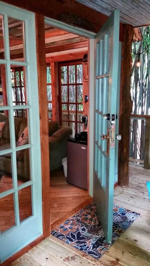 A cozy cabin interior with an open door, revealing wooden floors and a small fridge in the background.