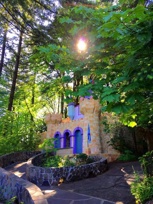 A whimsical stone castle surrounded by lush green trees, with sunlight filtering through the leaves.