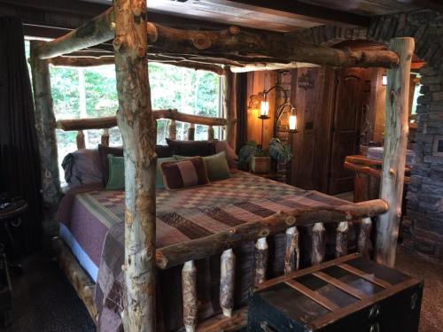 A rustic log cabin bedroom featuring a four-poster bed with a quilt, wooden accents, and warm lighting.