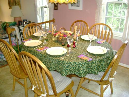 A round dining table set for a meal, featuring plates, glasses, and decorative items, surrounded by wooden chairs.