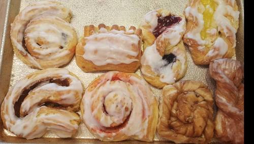 A tray of assorted pastries, including cinnamon rolls and fruit-filled danishes, all topped with icing.