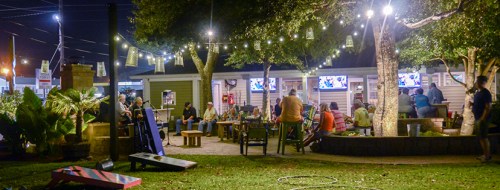 A lively outdoor gathering at night, with people socializing under string lights and trees in a cozy setting.