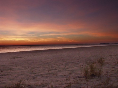 A serene beach at sunset, with soft sand and a colorful sky reflecting on the calm water.
