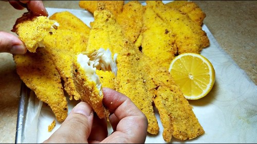 A plate of golden-breaded fish fillets with a hand holding a piece and a lemon slice nearby.