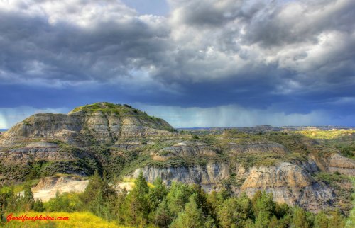 A dramatic landscape featuring layered hills under a stormy sky, with dark clouds and distant rain.