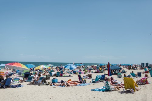 A crowded beach scene with colorful umbrellas, sunbathers, and people enjoying the sunny day by the ocean.