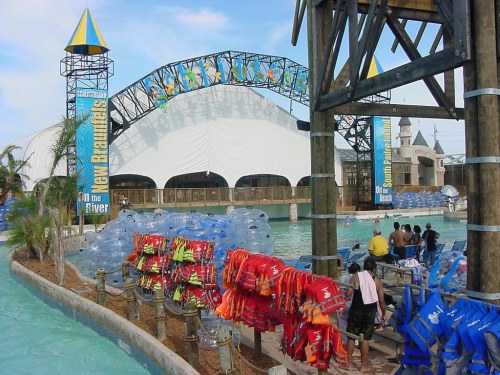 A water park scene featuring colorful life jackets, a lazy river, and a large stage in the background.