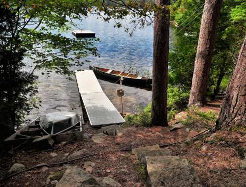 A serene lakeside scene with a wooden dock, a canoe, and trees surrounding calm waters.