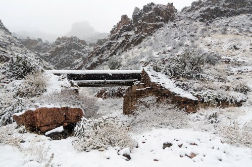 Snow-covered rocky landscape with a dilapidated stone structure and a pipe running through the scene.