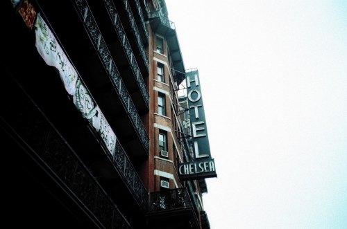 Sign for Hotel Chelsea on a brick building, featuring ornate balconies and a cloudy sky in the background.