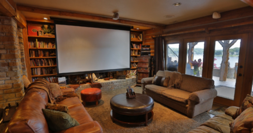 Cozy living room with a large screen, bookshelves, and comfortable seating, overlooking a scenic outdoor view.