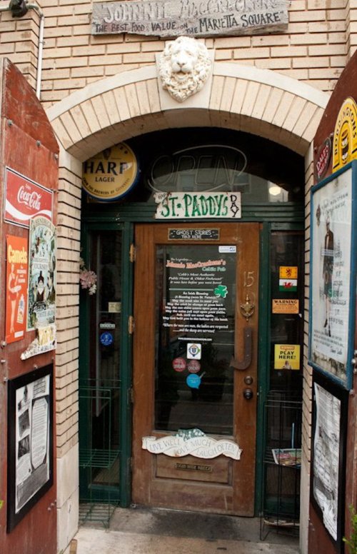 Entrance to Johnny McGorey's pub, featuring a wooden door with signs and posters, surrounded by brick walls.