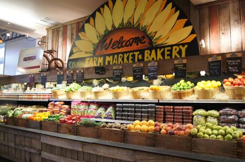 A vibrant farm market display featuring fresh fruits, vegetables, and baked goods under a sunflower welcome sign.