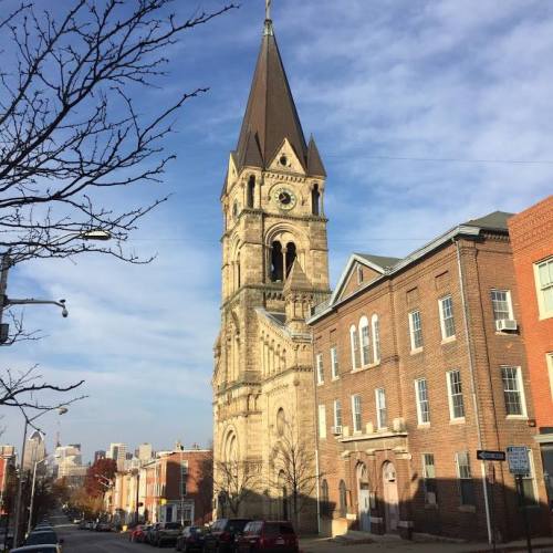 Historic church tower with a pointed roof, surrounded by residential buildings and a clear blue sky.