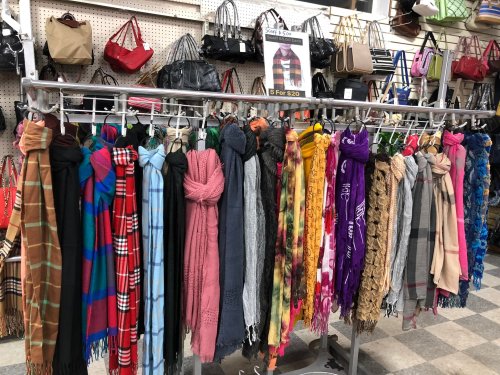 A display of colorful scarves hanging on a rack, with handbags visible in the background.