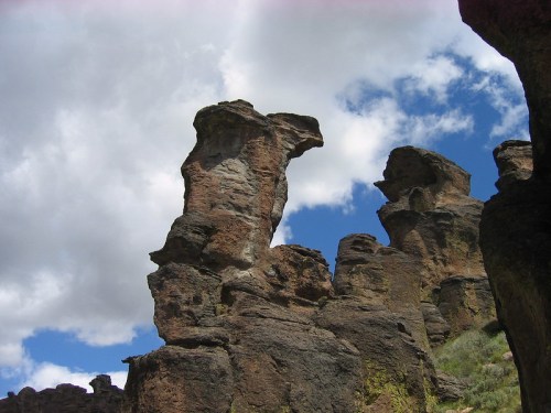 Rock formations rise against a blue sky with scattered clouds, showcasing unique shapes and textures.