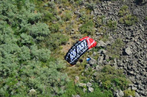 A parachute with "GO FAST" printed on it rests on rocky terrain surrounded by green vegetation.