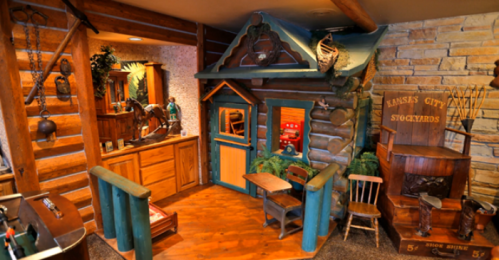A cozy, rustic room featuring a small log cabin playhouse, wooden furniture, and decorative items.