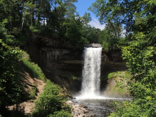A scenic waterfall cascading over a rocky cliff, surrounded by lush greenery and a clear blue sky.