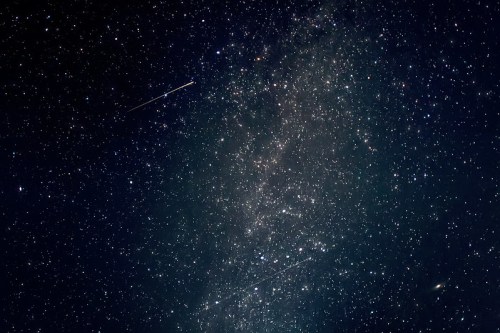 A starry night sky filled with countless stars and a few bright meteors streaking across the darkness.
