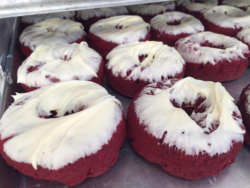 A tray of red velvet donuts topped with white icing, arranged neatly in a row.