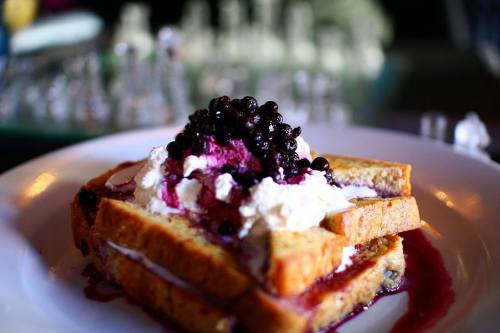 A stack of French toast topped with whipped cream and blueberries, drizzled with berry sauce on a white plate.