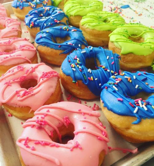 A tray of colorful donuts with pink, blue, and green icing, topped with sprinkles.