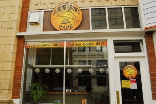 A storefront of Rising Trout Café featuring a sign, large windows, and a display of fresh coffee and pastries.