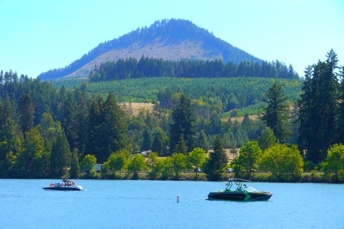 Two boats on a calm lake with a forested mountain in the background under a clear blue sky.