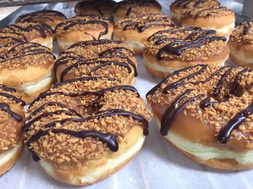 A close-up of donuts topped with crushed nuts and drizzled with chocolate, arranged on a tray.