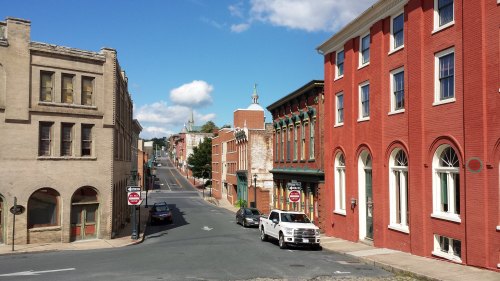 A view of a historic street with red brick buildings, parked cars, and a clear blue sky.