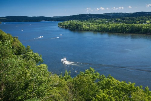 A scenic view of a river surrounded by lush greenery, with a boat cruising on the water under a clear blue sky.