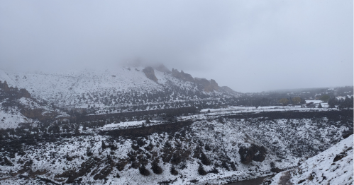 Snow-covered mountains and a valley shrouded in fog, with a river winding through the landscape.