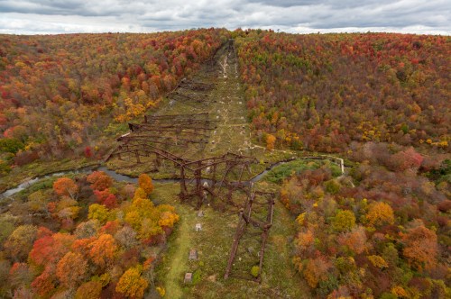 Aerial view of a forested landscape with vibrant autumn foliage and remnants of a rusted, abandoned structure.